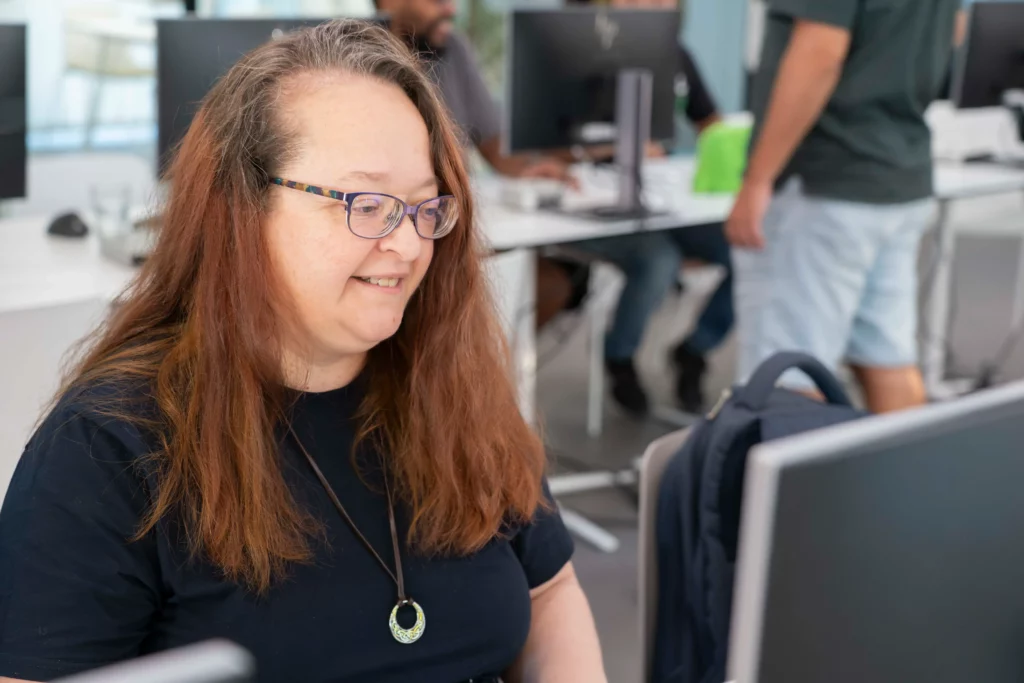 Trabajadora de WATA Factory sonriente y concentrada en su ordenador durante el taller de Kubernetes.