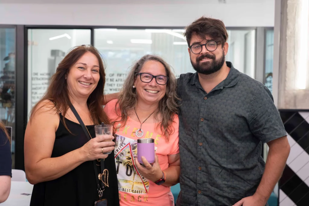 Dos mujeres y un hombre de WATA Factory sonríen mientras toman café en el descanso del All Hands.