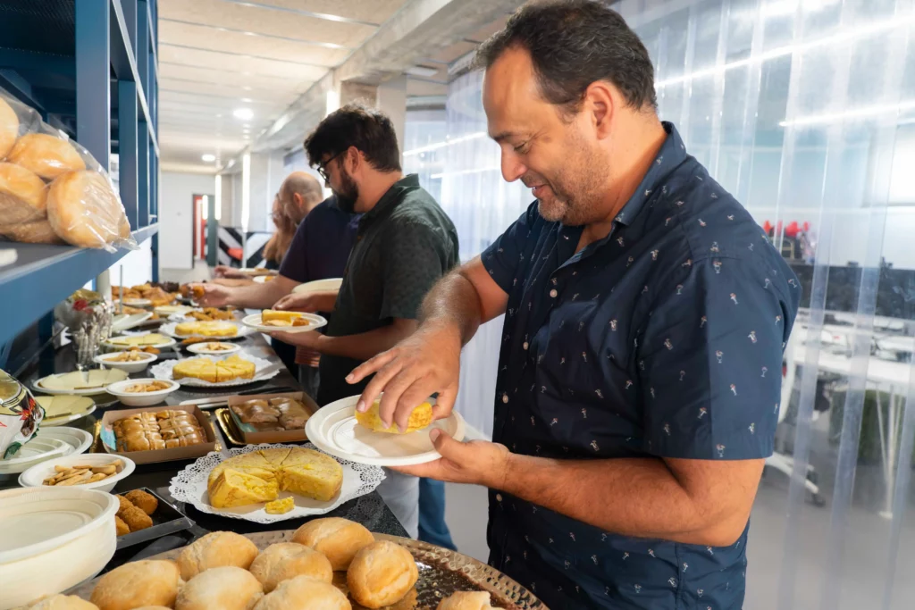 Mittagsbuffet bei WATA Factory mit Brot, Tortillas, Empanadas und Käse, während sich Kollegen Essen nehmen.