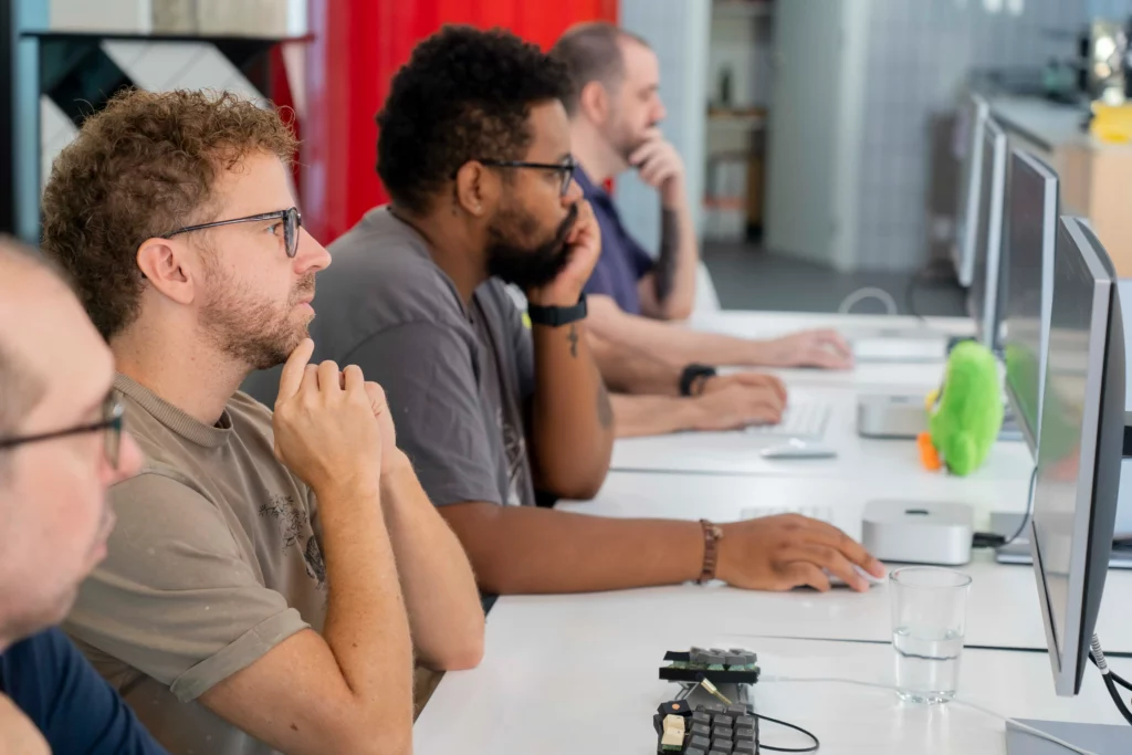 Fila de mesas con empleados de WATA Factory trabajando en portátiles mientras siguen las indicaciones de Laura Morillo-Velarde sobre Kubernetes.