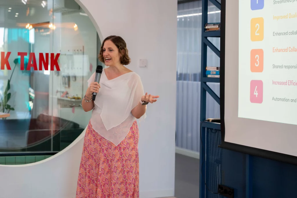 Laura Morillo-Velarde en el escenario de WATA Factory presentando sobre Kubernetes y DevOps con diapositivas proyectadas.
