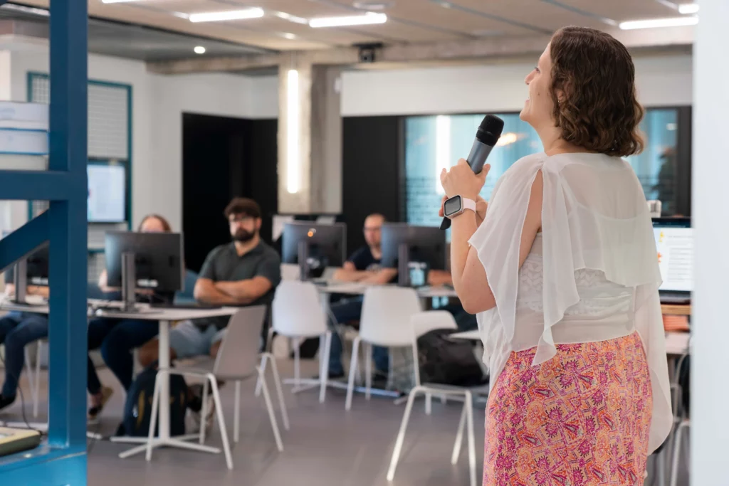 Rückansicht von Laura Morillo-Velarde mit WATA Factory-Mitarbeitern, die während des Kubernetes-Workshops an Laptops arbeiten.